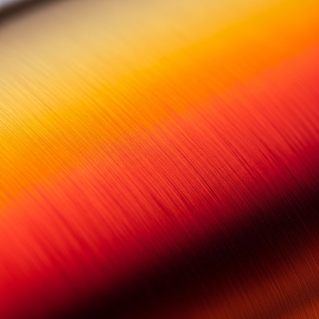 Close-up photograph of annealed copper-alloy surface showing orange and red thermal colour gradients from controlled heat treatment process