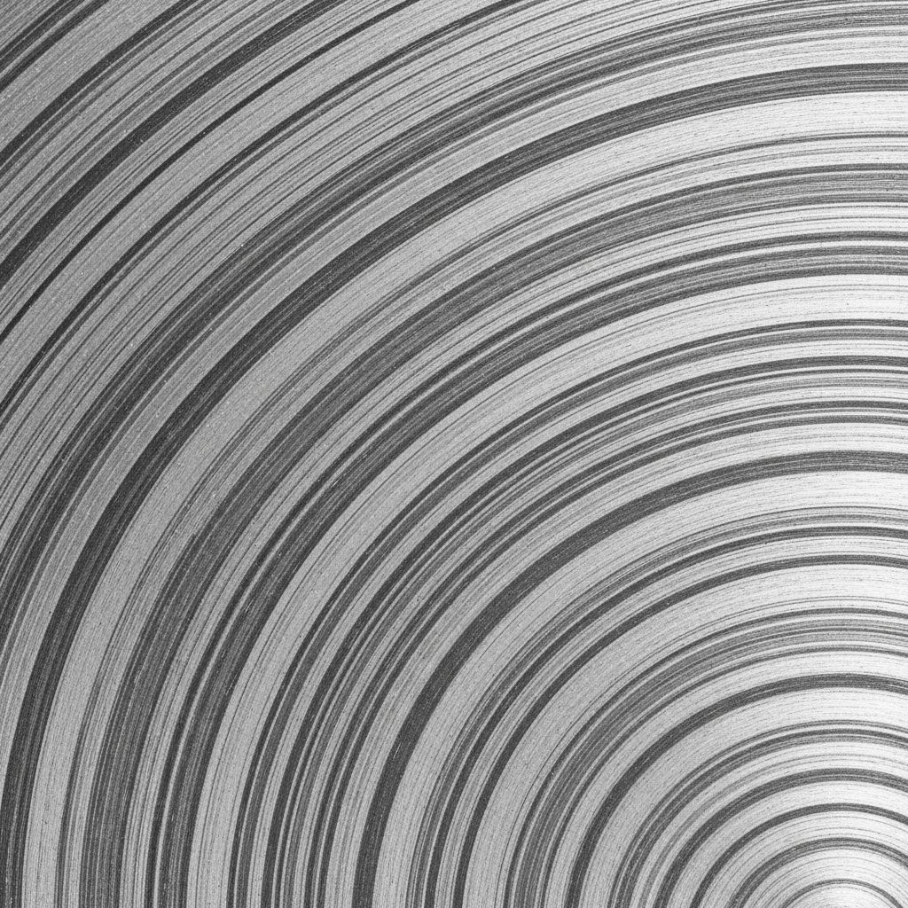 Polished cross-sectional slice of an aluminium alloy billet showing concentric grain flow patterns under directional studio lighting